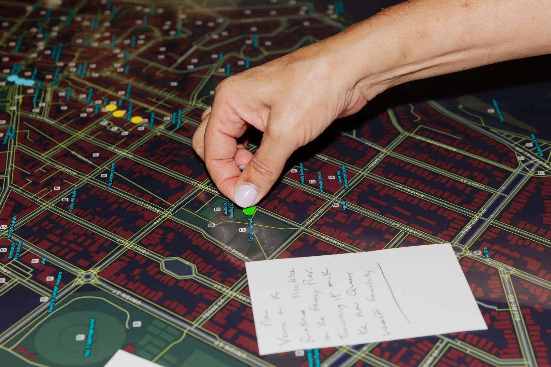A hand placing a coloured pin on a large printed map of Newcastle.